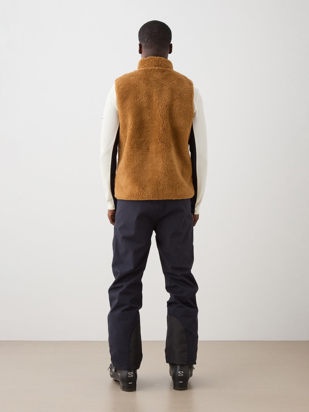 We Norwegians | FW25 | Mens Kebnekaise Vest_Cinnamon | Model wearing this fleece vest with front zipper opening, zipped chest pocket and side pockets -over an off-white top - paired with black ski pants | Shot against an off-white background | Back