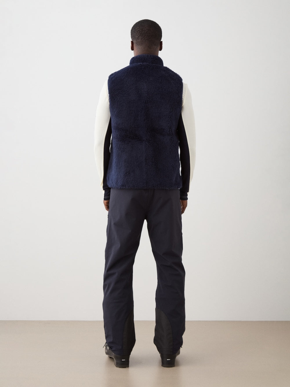 We Norwegians | FW25 | Mens Kebnekaise Vest_Navy blue | Model wearing this fleece vest with front zipper opening, zipped chest pocket and side pockets -over an off-white top - paired with black ski pants | Shot against an off-white background | Back