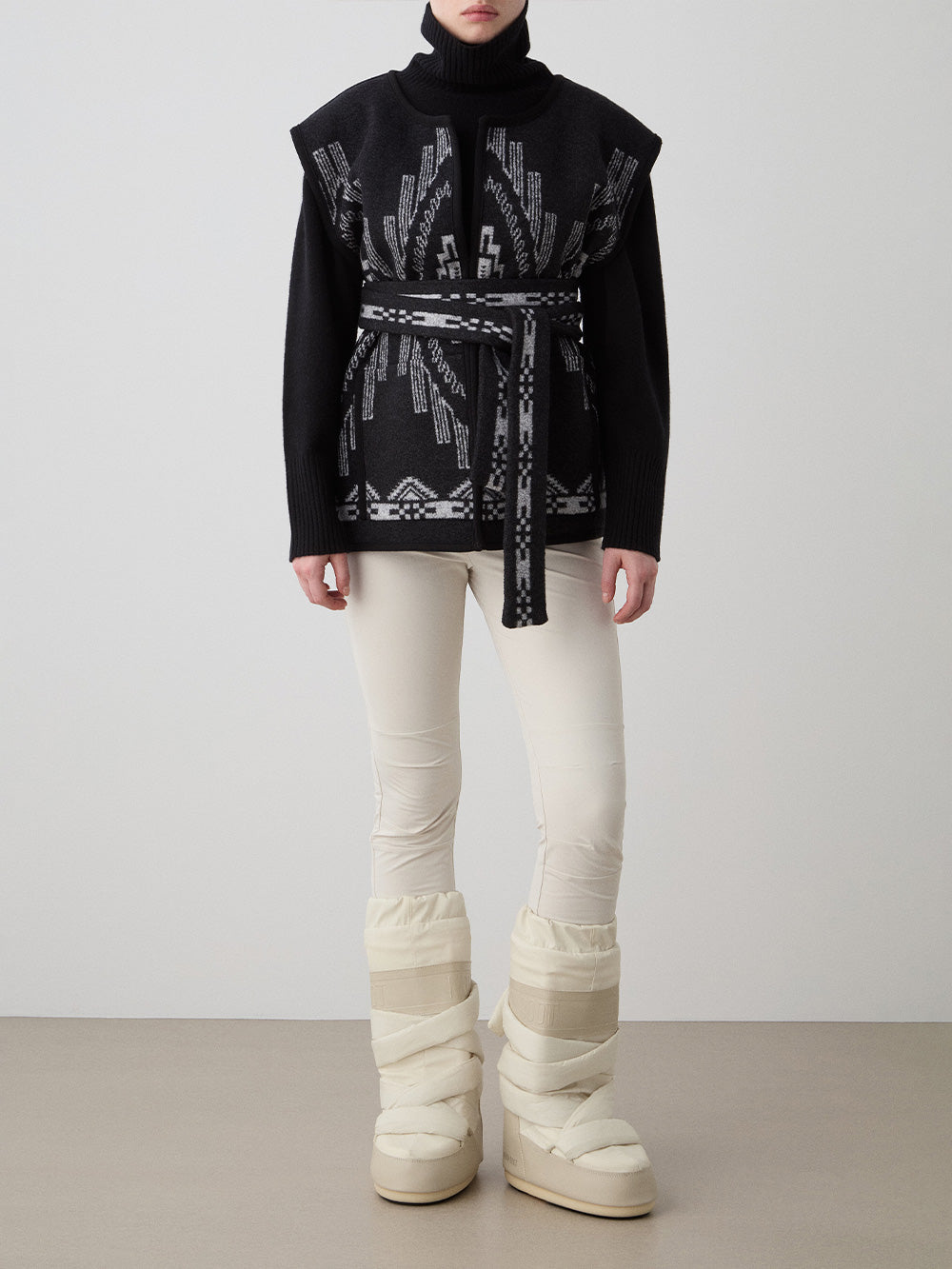 We Norwegians_FW25_Womens | Model is wearing the Pioneer vest | Black in color with a jacquard pattern | Vest has a matching belt to cinch the waist | Front view on a white background