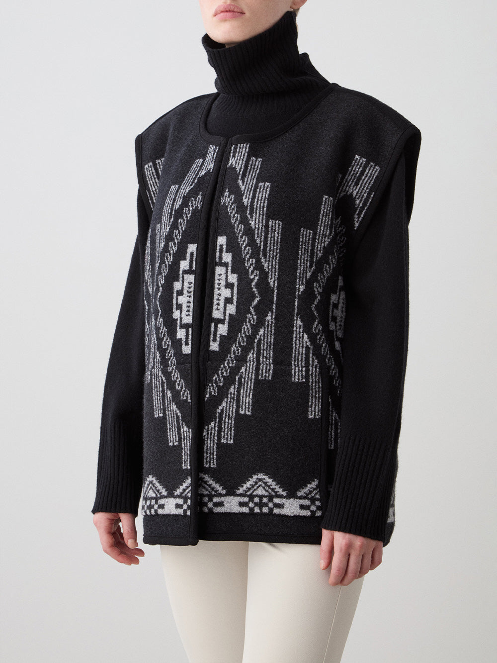 We Norwegians_FW25_Womens | Model is wearing the Pioneer vest | Black in color with a jacquard pattern | Vest has a matching belt to cinch the waist | Photograph shows the details of the garment on a white background