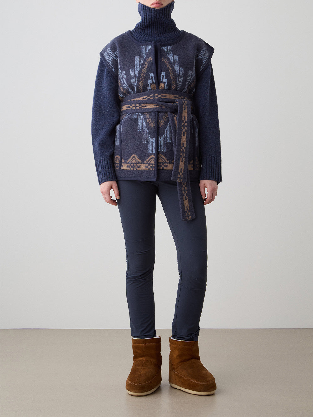 We Norwegians_FW25_Womens | Model is wearing the Pioneer vest | Navy blue in color with a jacquard pattern | Vest has a matching belt to cinch the waist | Front view on a white background