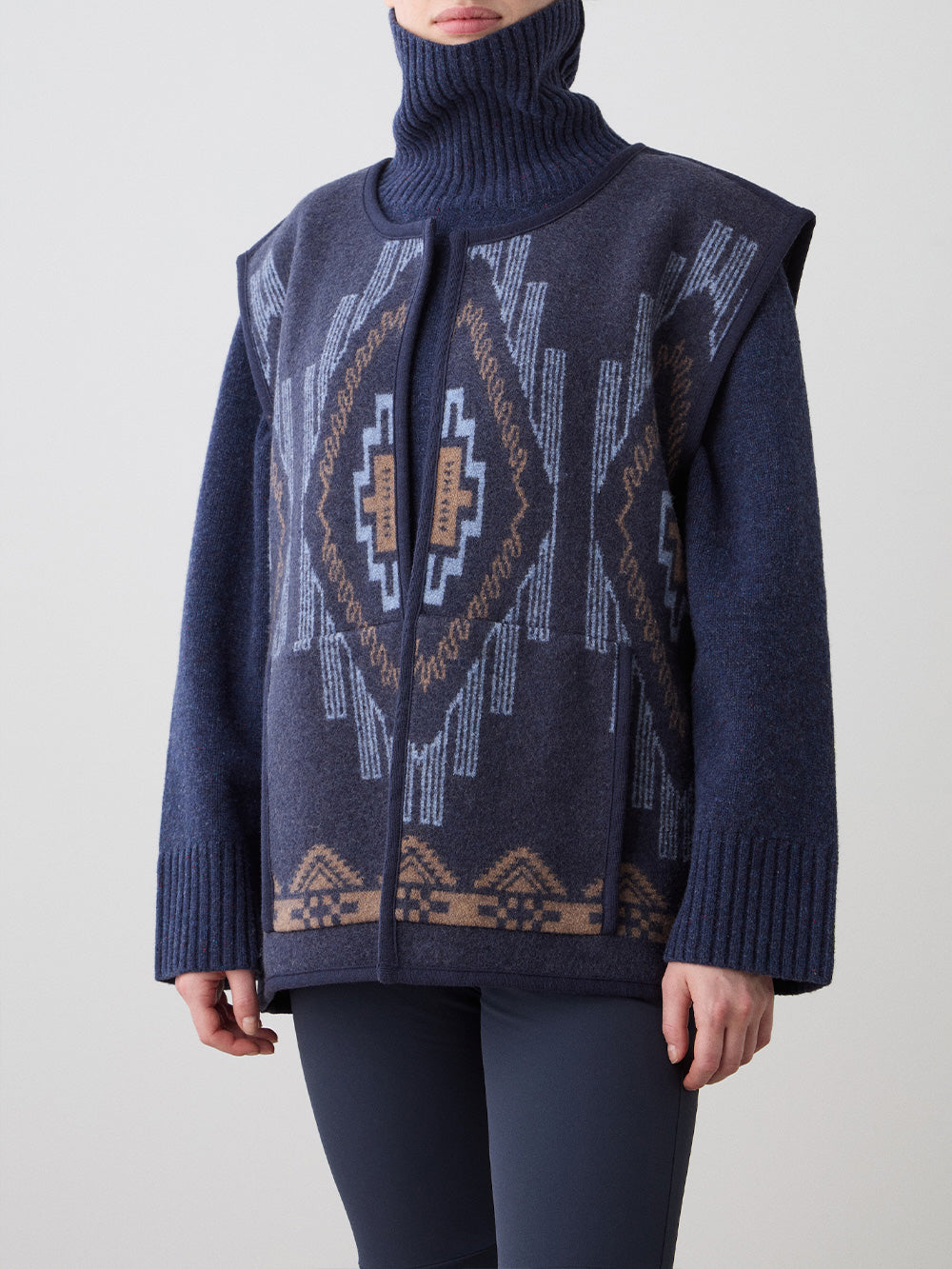 We Norwegians_FW25_Womens | Model is wearing the Pioneer vest | Navy blue in color with a jacquard pattern | Vest has a matching belt to cinch the waist | Photograph is showing the details of the garment on a white background