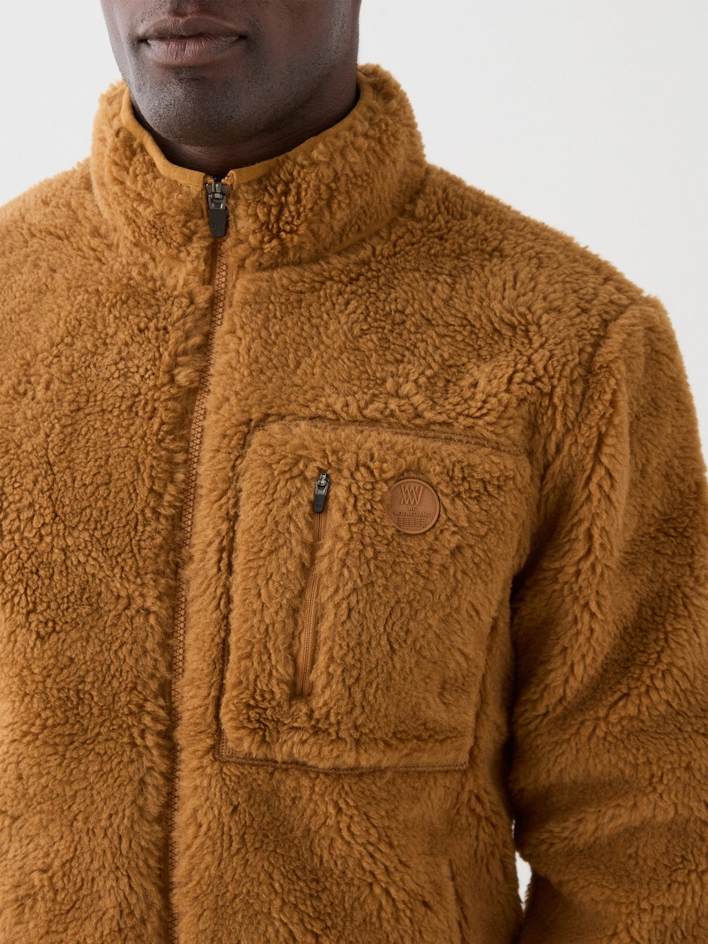 We Norwegians | FW25 | Mens Kebnekaise Jacket_Cinnamon | Model wearing this fleece jacket with front zipper opening, zipped chest pocket and side pockets - paired with black ski pants | Shot against an off-white background | Close-up