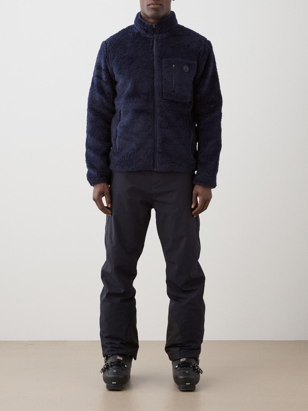 We Norwegians | FW25 | Mens Kebnekaise Jacket_Navy blue | Model wearing this fleece jacket with front zipper opening, zipped chest pocket and side pockets - paired with black ski pants | Shot against an off-white background | Front