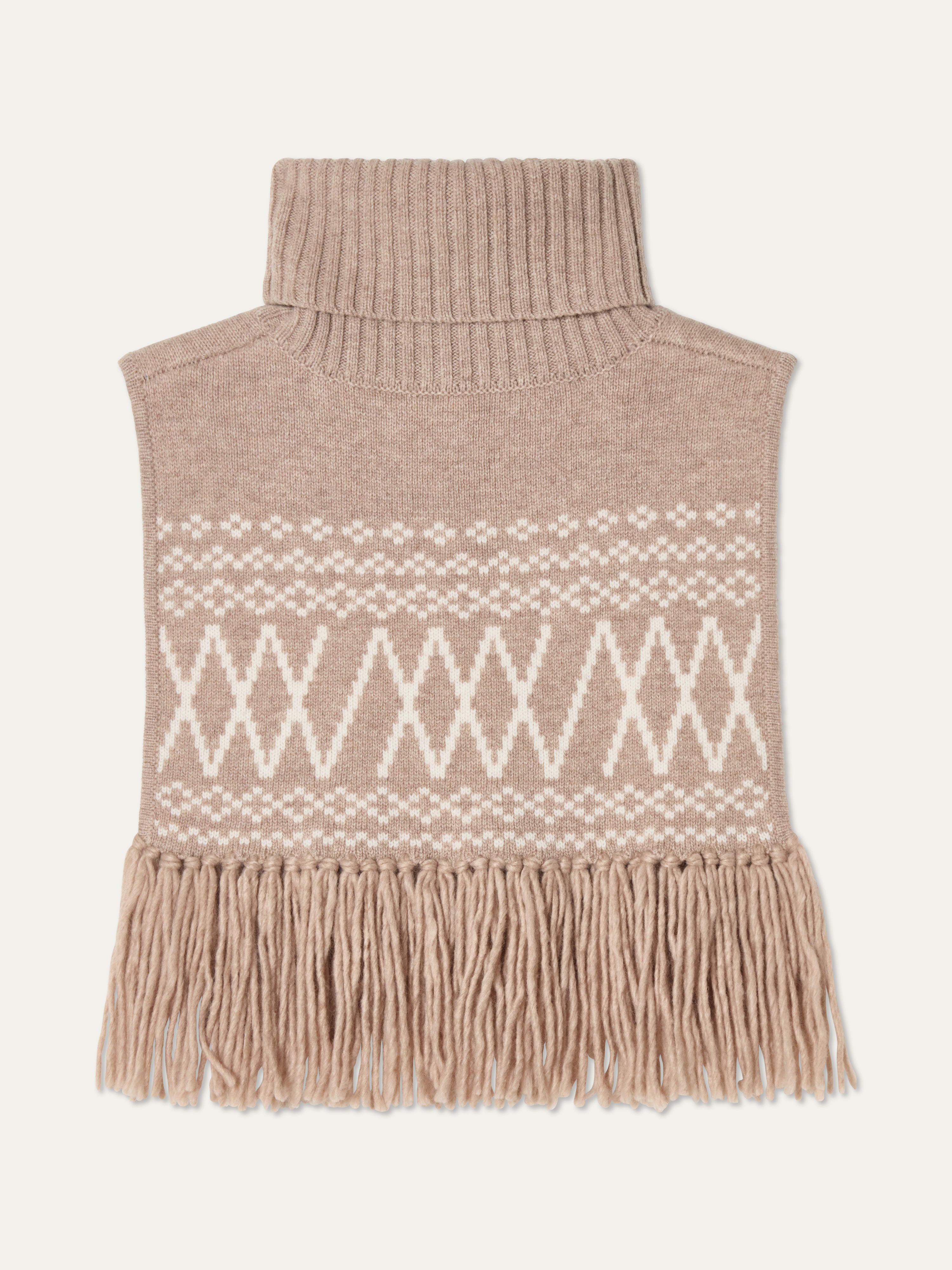 We Norwegians | FW25 | Setesdal Bib_Sand | A knitted bib with a turtle neck and fine fringes at the hem against an off-white background